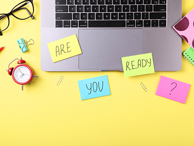 Open laptop, glasses, alarm clock, notebooks, paperclips and bulldog clip with post-it notes that have the words 'are you ready?' written on them.. Link to Are you “exam fit”? May 2025.