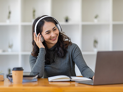 Student in an online session (with a laptop and note book, wearing headphones). Link to Succeed@Tees workshops return in Semester 3.