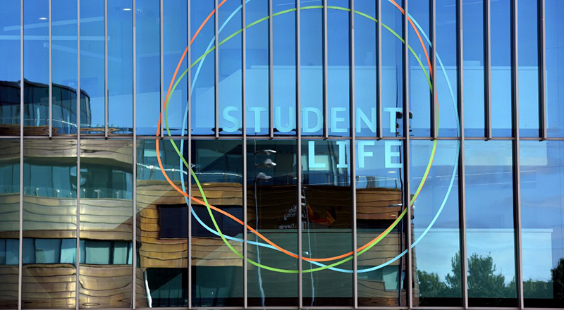 Student Life Building, in sunshine, with the Curve reflected in the window.