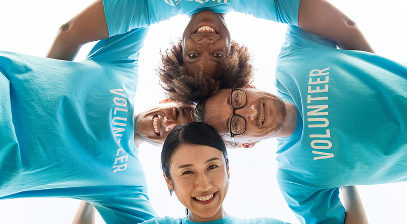 Group of people in a circle, heads together, in volunteer t-shirts.  Photo taken from below.