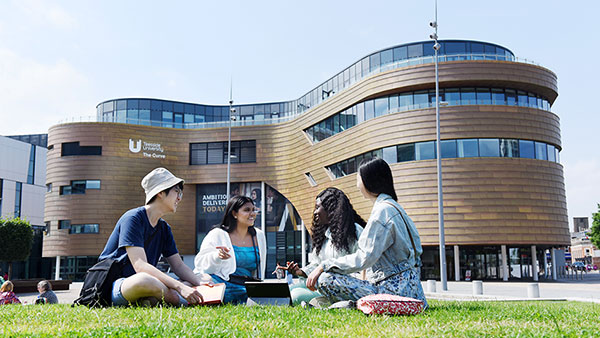 International students sit in the grass of campus heart