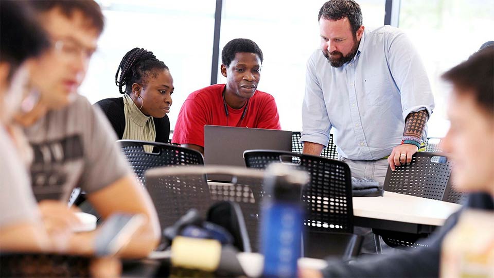 University staff and researchers talking around a laptop.