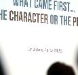 People watching a big screen that states What Came First...The Character of the Plot?