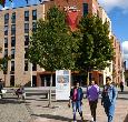 A group of students walk across campus with the exterior of the Cornell Quarter building at Teesside University visible behind them.
