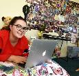 A student lies on her bed using a laptop in a bedroom at Parkside Halls