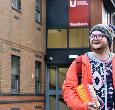 A student holding books walking outside the Woodlands Hall student accommodation building at Teesside University