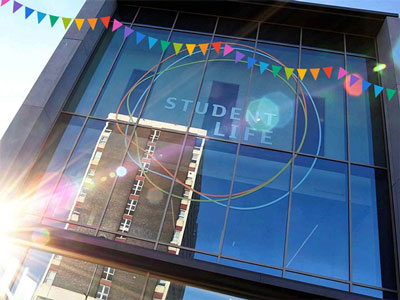 Student Life Building window with a graphic of festival flags across the top. The window has the words 