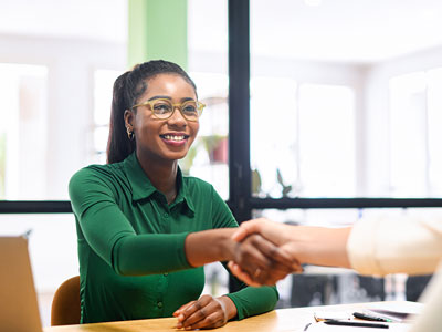 An image of a person shaking hands with someone, across a desk. . Link to Graduate Support Week, 29 June - 3 July 2026.