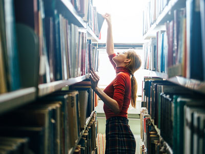 An image of a person reaching upwards to retrieve books from a book shelf. Link to New and improved Discovery.