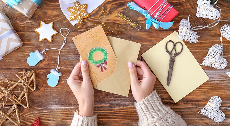 Woman with envelope and handmade Christmas card at wooden table