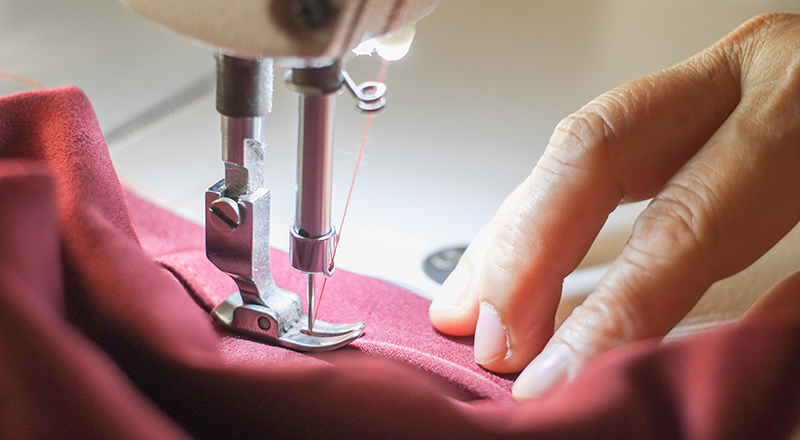 Someone using a sewing machine to hem a  garment - photo shows hand, fabric and sewing machine foot/ needle.