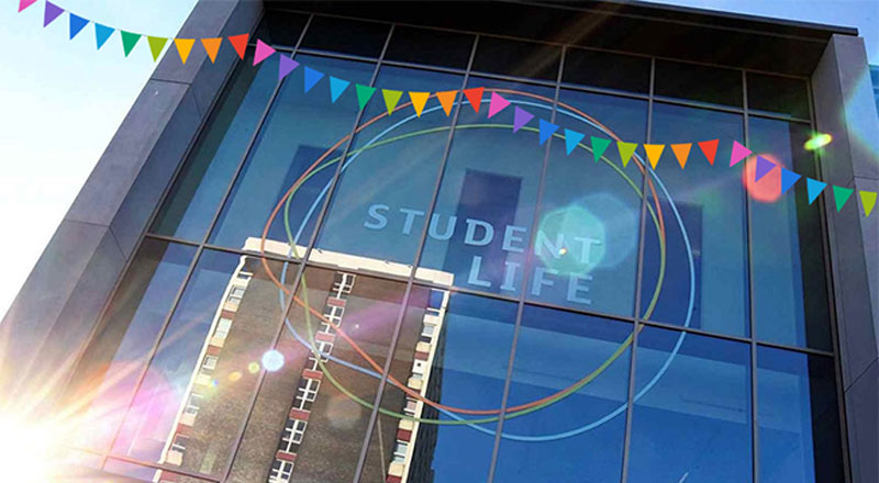 Student Life Building window with a graphic of festival flags across the top. The window has the words 