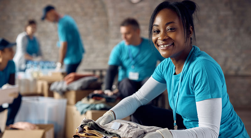 An image of a volunteer carrying clothes and smiling. Other volunteers can be seen in the background. 