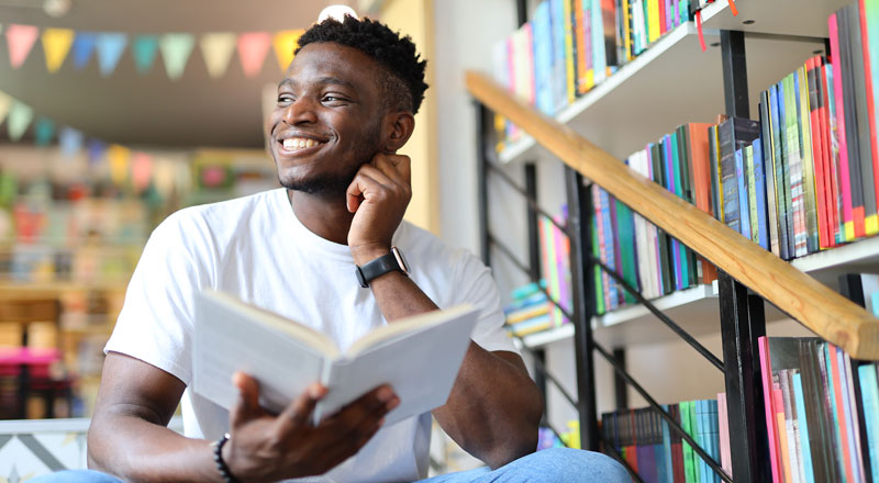 An image of a person smiling whilst holding a book.. Link to An image of a person smiling whilst holding a book..