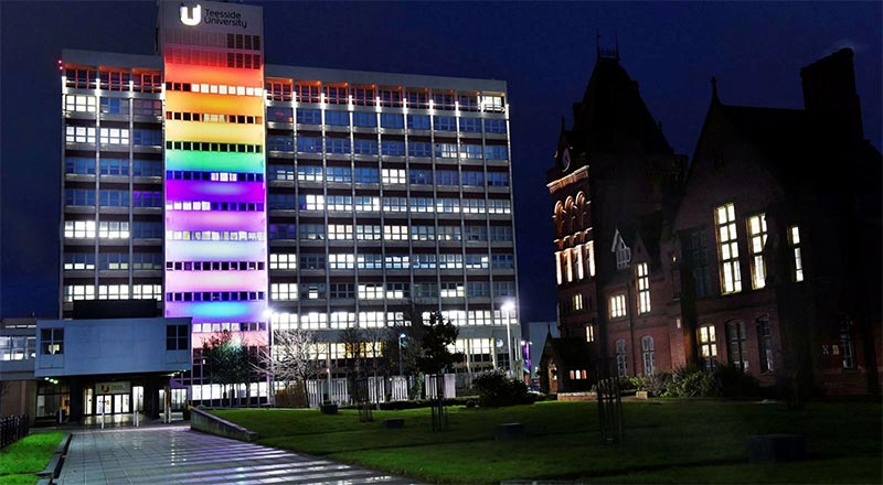 University building illuminated in rainbow colours to celebrate and support the LGBTQ+ community. Link to Another World: celebrating local LGBTQ+ storytelling.
