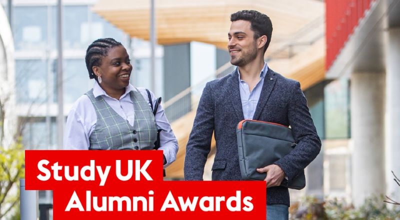 Two international graduates walking together on a university campus beside Study UK Alumni Awards branding