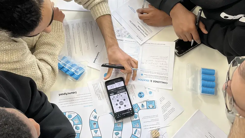 Students in a brainstorming session, collaborating with print outs and a mobile device