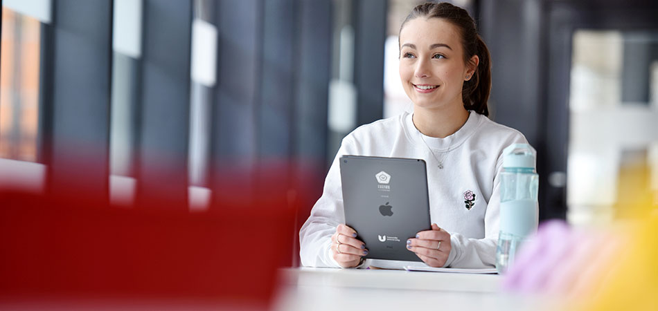 Postgraduate student studying at a table using a tablet in a university learning space