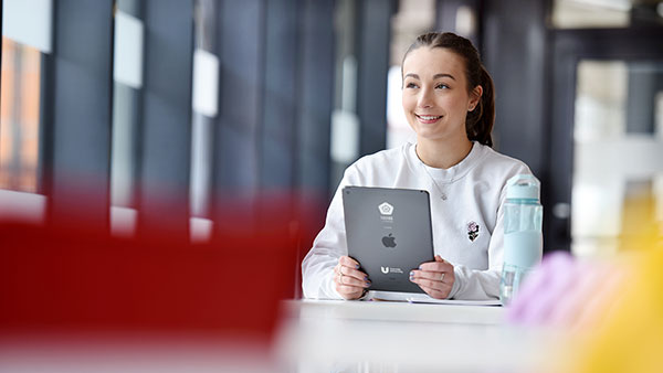 Postgraduate student studying at a table using a tablet in a university learning space