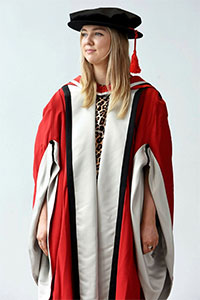 A red/grey gown, with Teesside University hood, cloth bonnet with red tassel