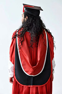 A red gown, with Teesside University hood, black mortar board with red tassel