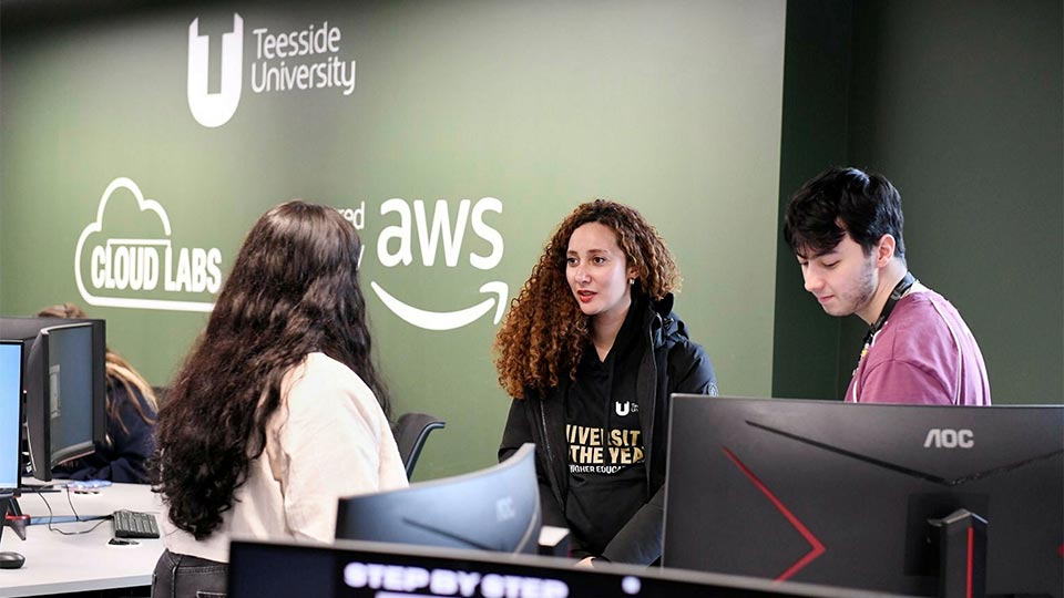 Digital life lab, with AWS and Cloud labs logo on the wall. Staff are having a conversation close to computers.