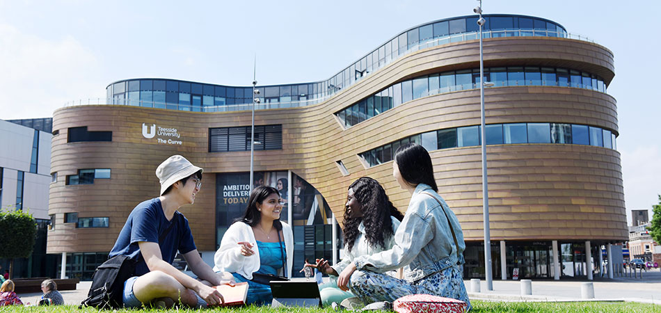 International students sit in the grass of campus heart