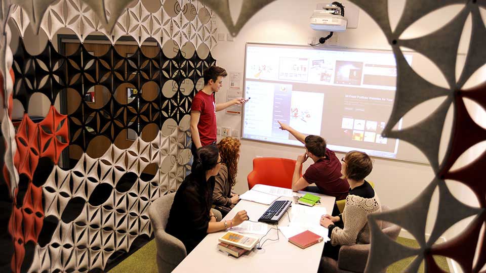 Students in a classroom pointing at a large screen