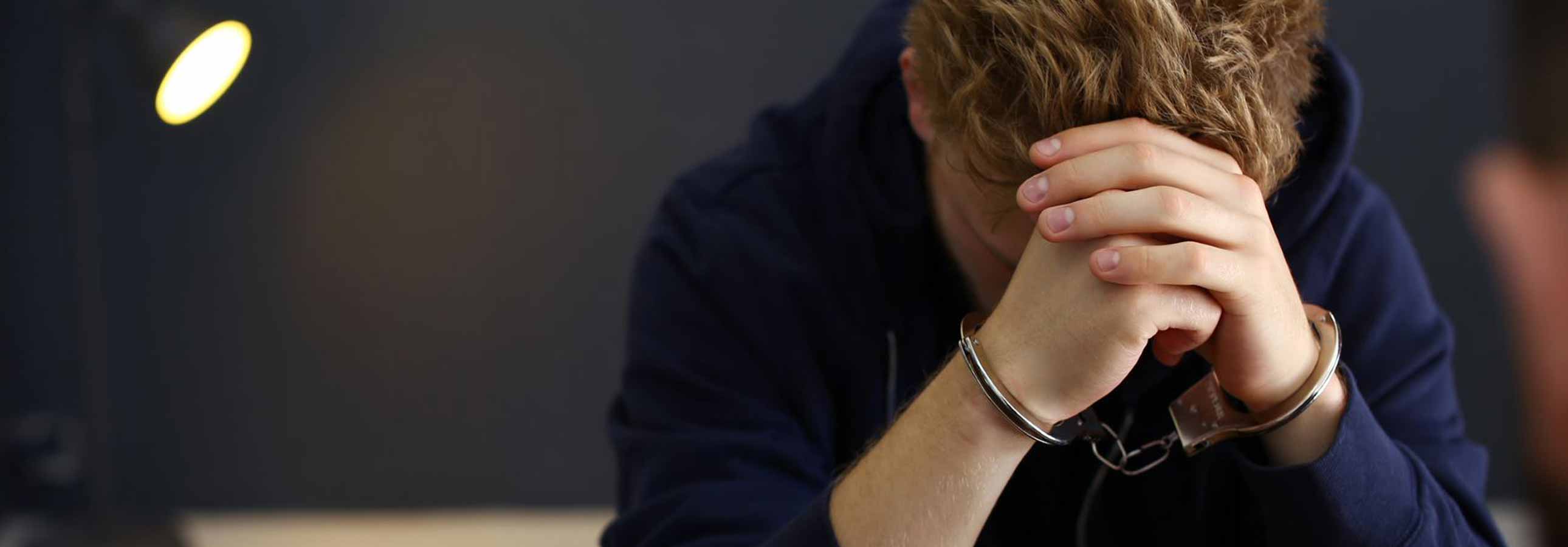 Man wearing handcuffs sitting in a jail cell, appearing vulnerable