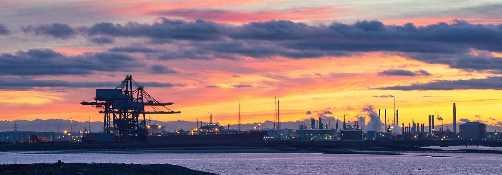 Industrial facilities and shipping containers at a busy port, with cranes and infrastructure in view