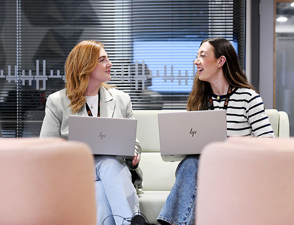Two students sitting and talking with laptops open in front of them
